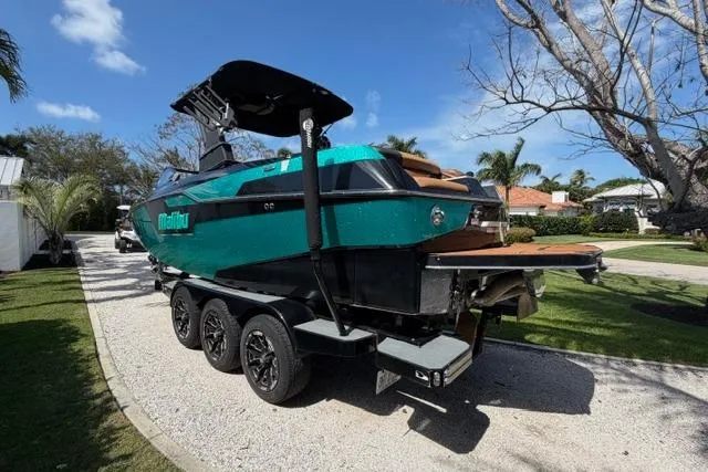 Slide: The Image of 2021 Malibu M240 boat on trailer, parked outdoors under clear blue sky. - 3
