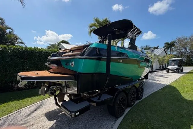 Slide: The Image of 2021 Malibu M240 boat on trailer, parked in sunny driveway with palm trees. - 4