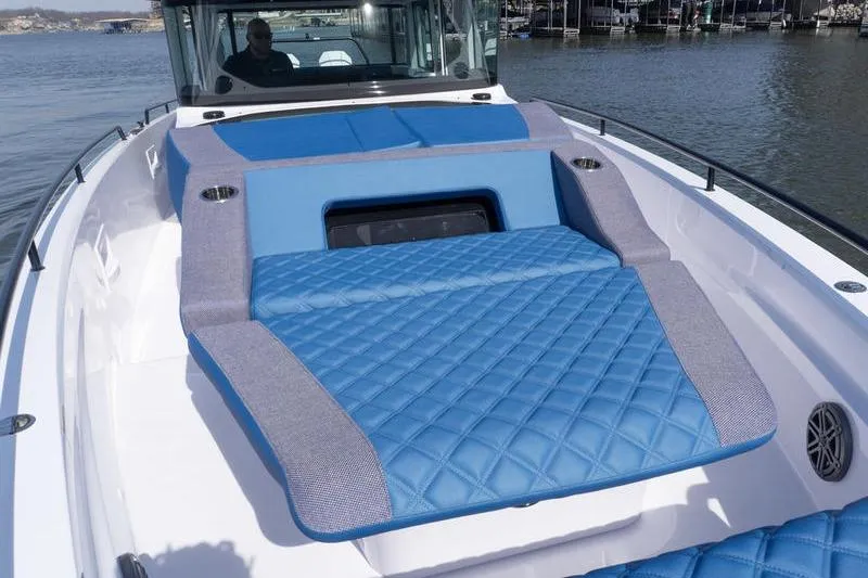 Slide: The Image of 2026 Axopar 37 XC Cross Cabin with blue quilted sunbed on deck, docked by the water. - 8