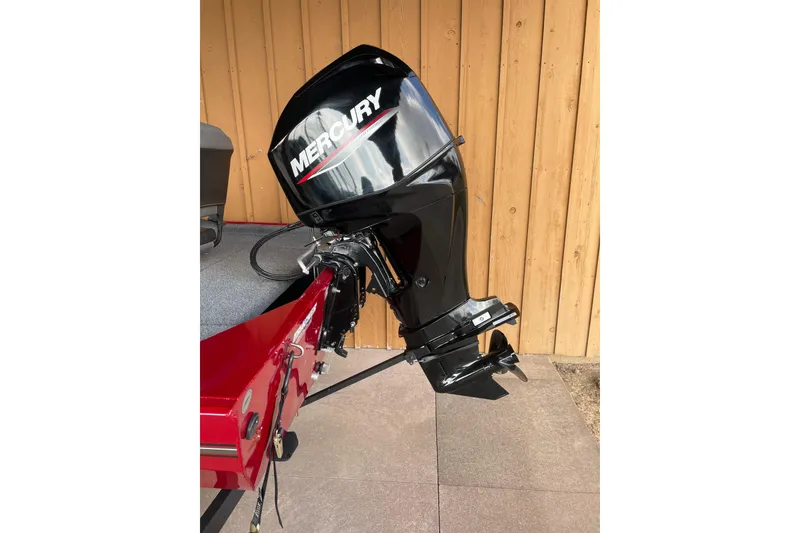 Slide: The Image of 2024 Tracker Bass Tracker Classic XL with Mercury outboard motor, parked by wooden wall. - 2