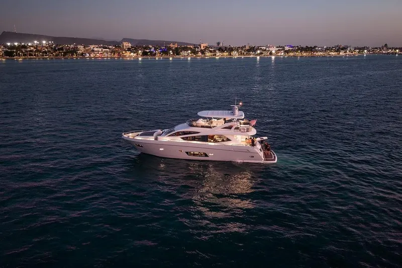 Slide: The Image of Luxurious 2012 Sunseeker Manhattan 73 yacht cruising at dusk near a vibrant coastline. - 4