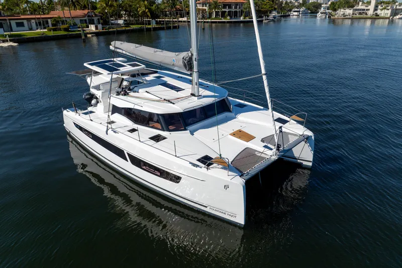 Slide: The Image of 2025 Fountaine Pajot FP41 Catamaran sailing on calm waters near waterfront homes. - 2