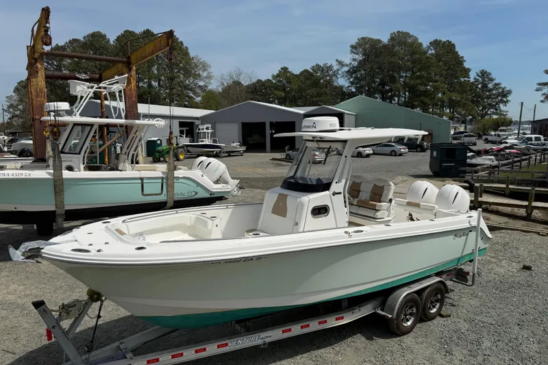 Slide: The Image of 2019 Edgewater 262CC boat on trailer by waterfront dock, surrounded by trees and buildings. - 19