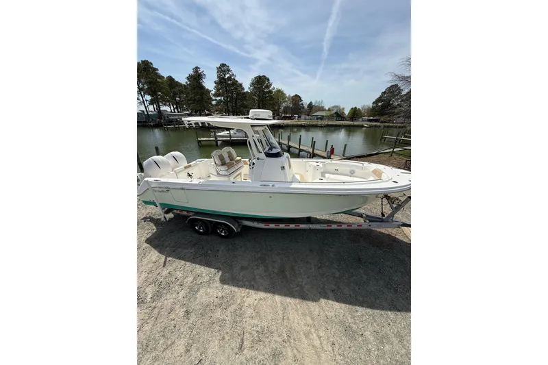 Slide: The Image of 2019 Edgewater 262CC boat with dual outboard motors on a trailer, parked outdoors. - 21