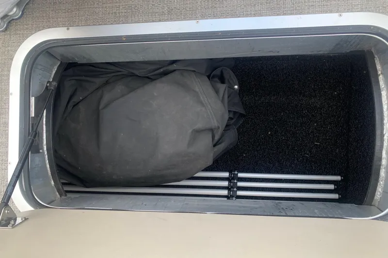 Slide: The Image of Storage compartment in a 2022 Barletta C22UC boat, containing a black cover and metal poles. - 13