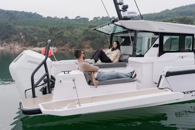 Slide: The Image of 2027 Axopar 38 Cross Cabin with people relaxing on deck, scenic water backdrop. - 10