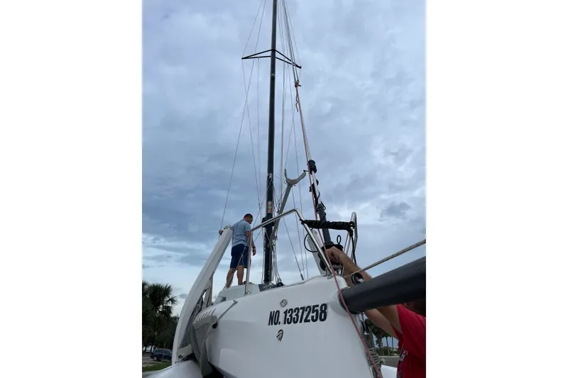 The Image of 2021 Corsair 880 Sport sailboat with people adjusting rigging under cloudy sky. - 1