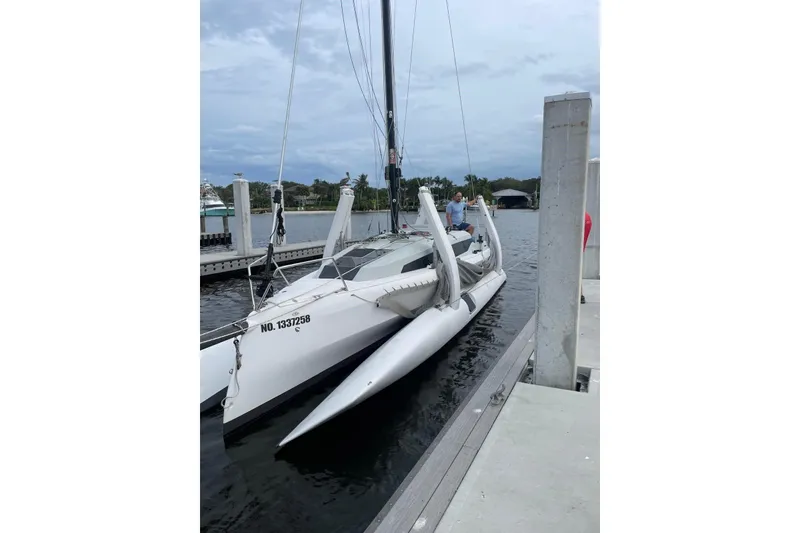 Slide: The Image of 2021 Corsair 880 Sport trimaran docked at a marina under cloudy skies. - 2