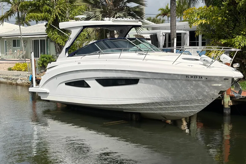 The Image of 2022 Regal 33 XO boat docked by a waterfront home, surrounded by palm trees. - 1