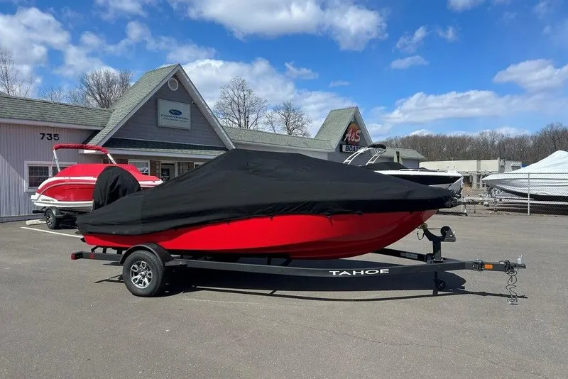 Slide: The Image of 2025 Tahoe T18 boat with cover on trailer, parked outside dealership under blue sky. - 15