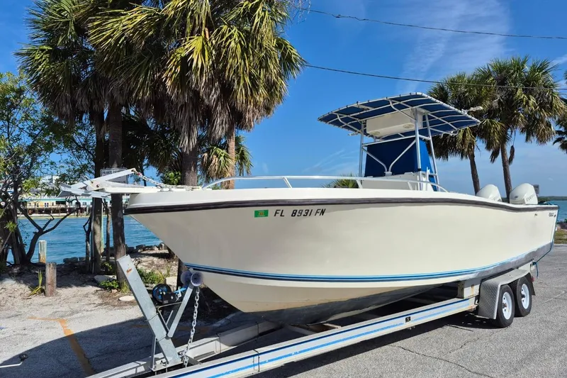 The Image of 1987 Mako 261 Center Console boat on trailer, parked near palm trees by the water. - 1