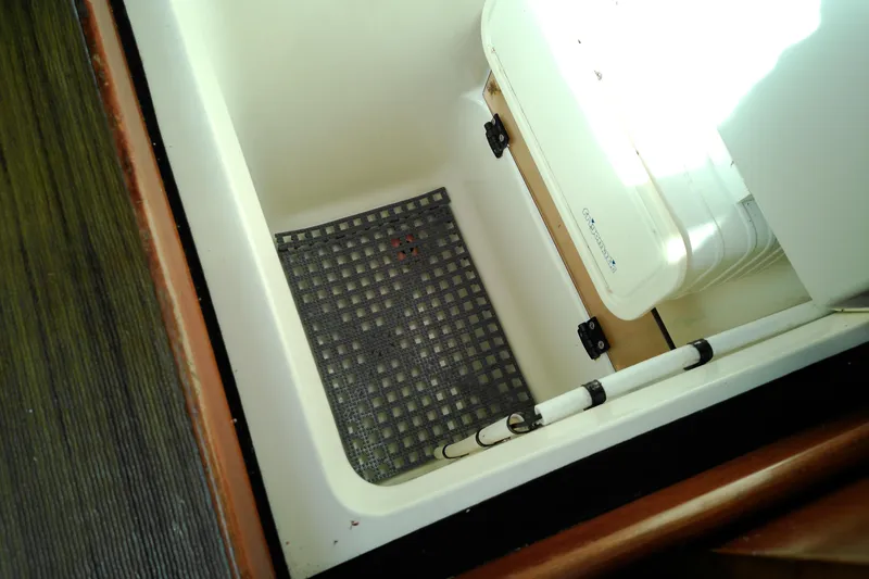 Slide: The Image of Storage compartment in a 1993 Beneteau First 310 sailboat, featuring a grid mat and white container. - 38