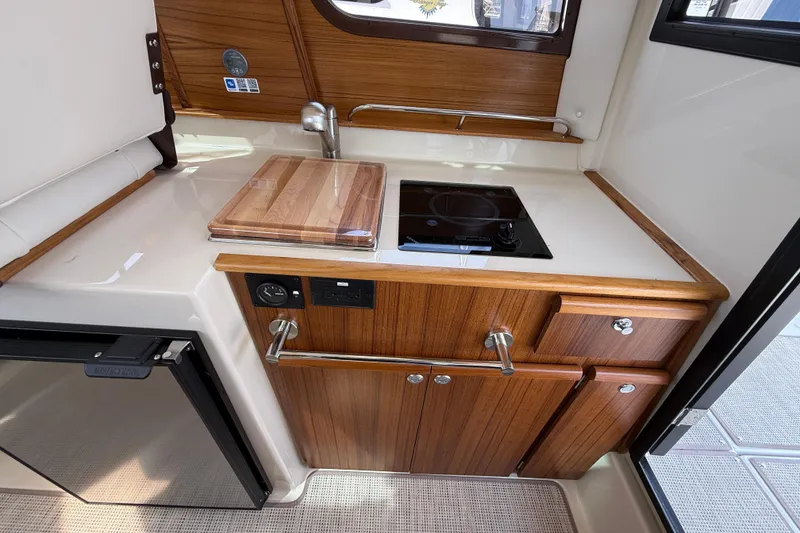 Slide: The Image of 2026 Ranger Tugs R-25 galley with wood cabinetry, sink, and stovetop. - 10