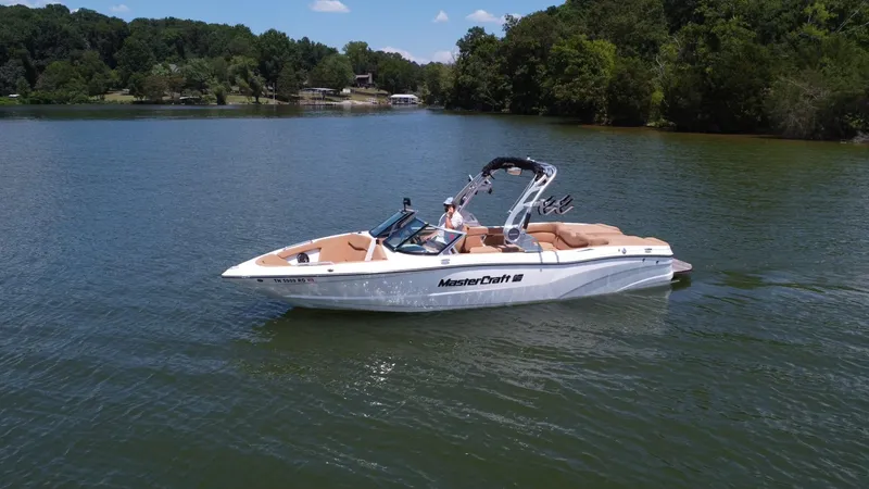 Slide: The Image of 2021 MasterCraft XT25 boat cruising on a serene lake with lush green surroundings. - 3