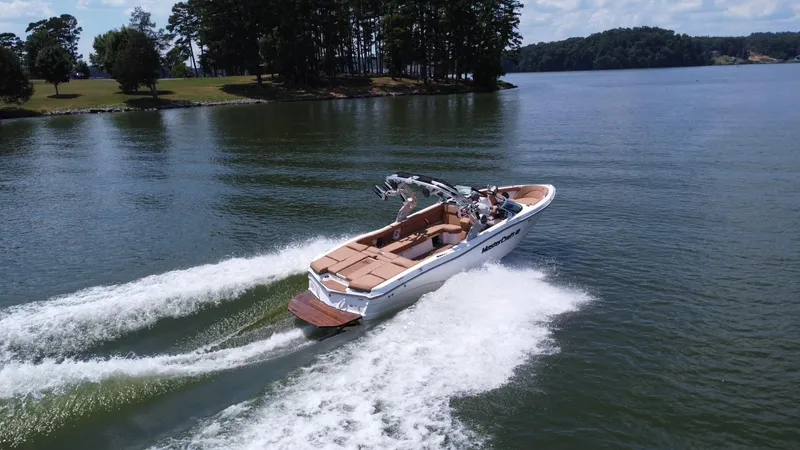 Slide: The Image of 2021 MasterCraft XT25 boat cruising on a lake with lush green shoreline. - 7