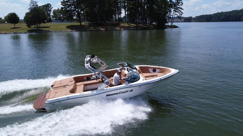 Slide: The Image of 2021 MasterCraft XT25 boat cruising on a lake with lush green surroundings. - 8