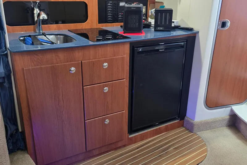 Slide: The Image of 2007 Bayliner 325 interior kitchen with wood cabinets, sink, and compact refrigerator. - 28
