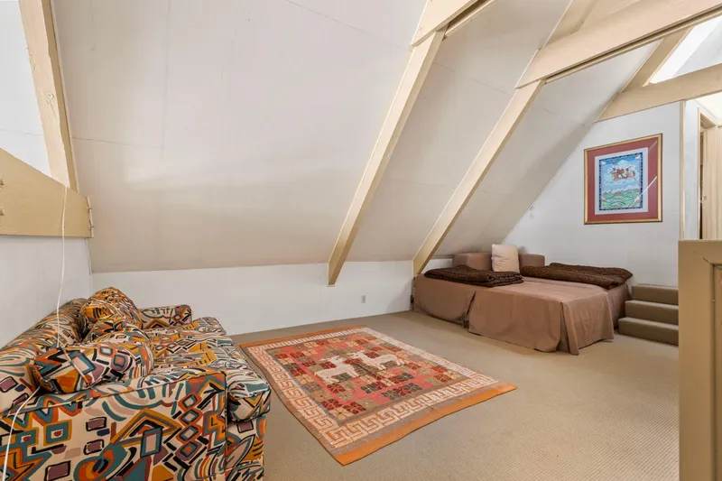 Slide: The Image of A-frame attic room with patterned sofa, colorful rug, and bed, in a 1976 custom boathouse. - 22