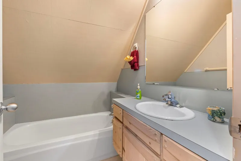 Slide: The Image of Small bathroom with angled ceiling, bathtub, wooden vanity, and large mirror in a 1976 custom boathouse. - 23