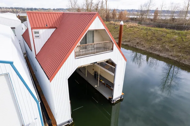 Slide: The Image of Custom 1976 boathouse with red roof, docked on calm water, surrounded by trees. - 37