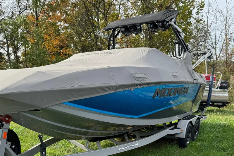 Slide: The Image of 2023 Moomba Mojo boat covered on trailer, parked on grass with trees in background. - 1