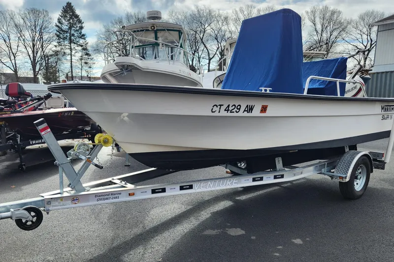 The Image of 1999 Maritime Skiff 1690 on trailer, parked outdoors with other boats. - 0