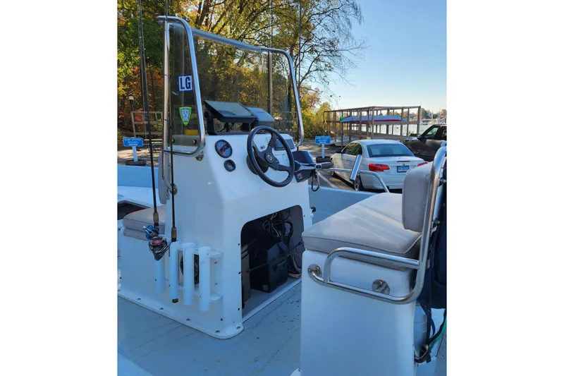 Slide: The Image of 1999 Maritime Skiff 1690 boat interior with steering console and seating, docked near a parking area. - 49