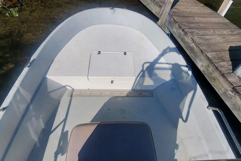 Slide: The Image of 1999 Maritime Skiff 1690 boat interior near wooden dock, showing seating and storage. - 7