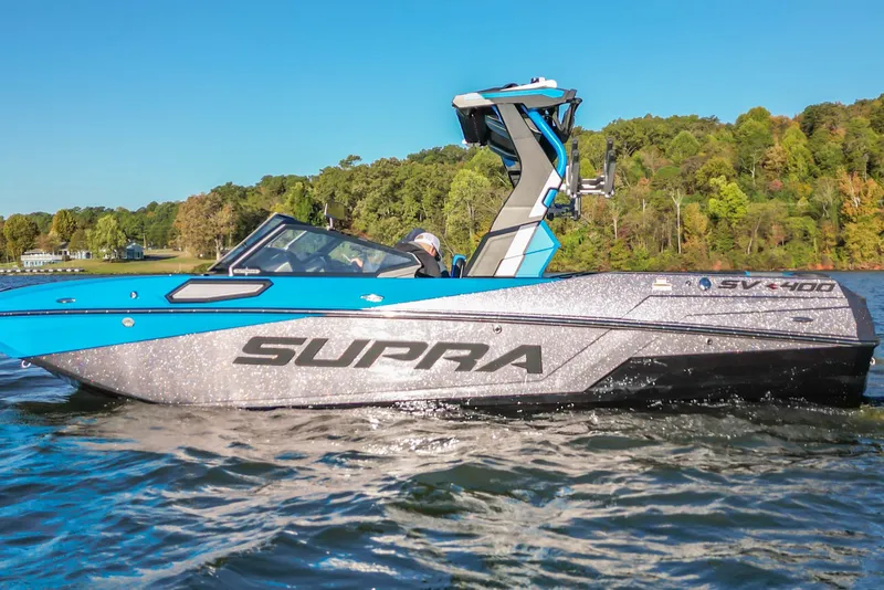 Slide: The Image of 2024 Supra SV 400 boat cruising on a lake with lush green shoreline. - 10