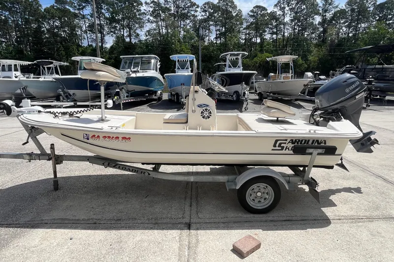 Slide: The Image of 2015 Carolina Skiff JV15CC boat on trailer, parked outdoors with other boats in background. - 4