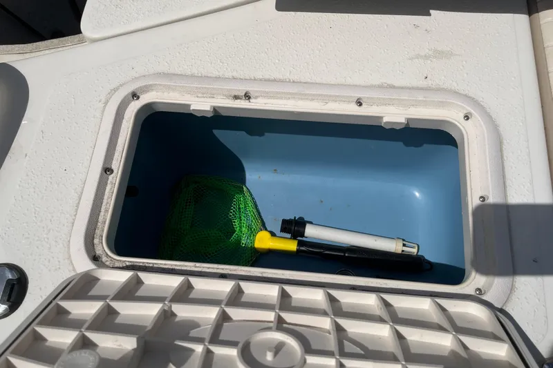 Slide: The Image of Open storage compartment on 2015 Carolina Skiff JV15CC boat with net and tools inside. - 9