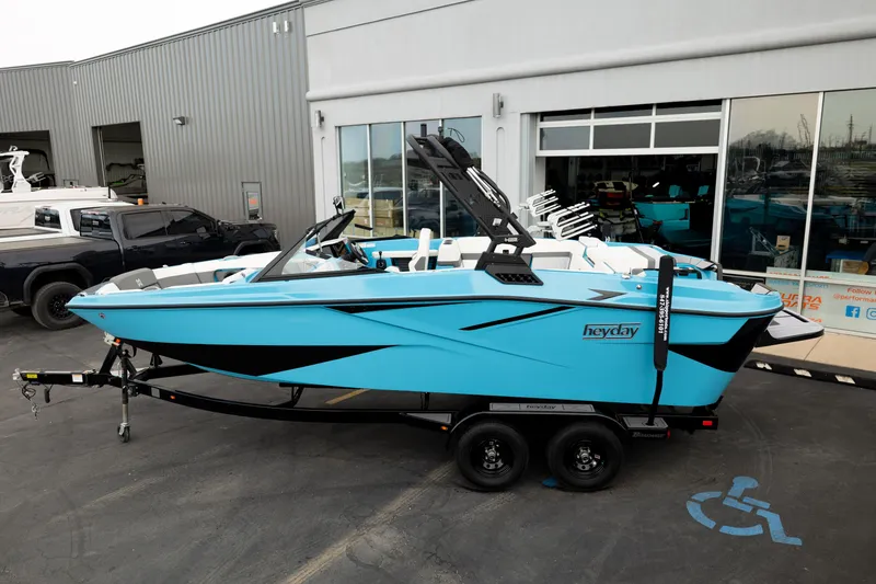 Slide: The Image of 2023 Heyday H22 boat in vibrant blue on a trailer outside a showroom. - 3