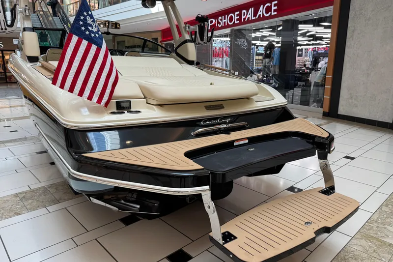 Slide: The Image of 2026 Chris-Craft Sportster 25 boat displayed indoors with American flag, near Shoe Palace store. - 23