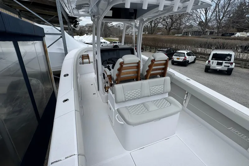 Slide: The Image of 2026 Jupiter 30 boat with cushioned seating and sleek design in a parking area. - 12