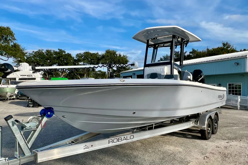 Slide: The Image of 2026 Robalo 246 Cayman boat on trailer, parked outdoors near a blue building. - 4