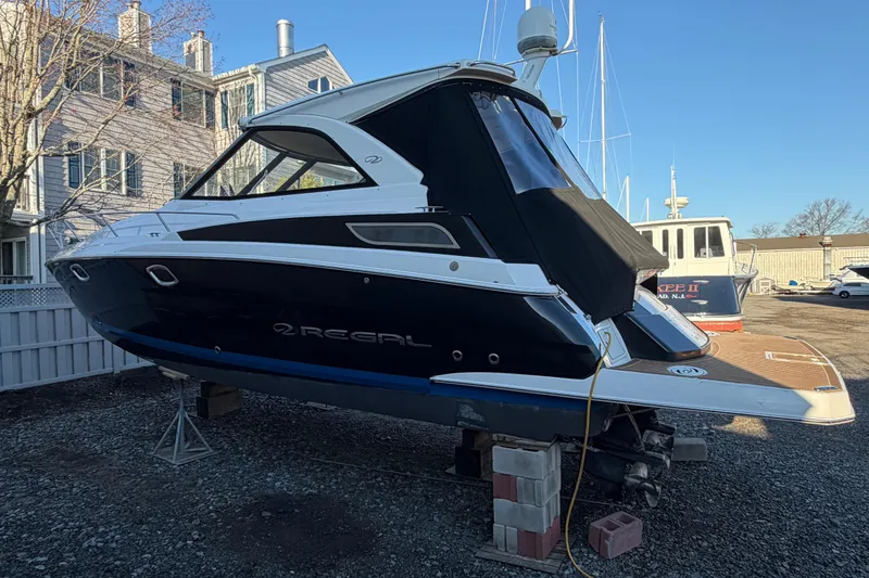 Slide: The Image of 2013 Regal 35 Sport Coupe boat on dry dock, black hull, marina background. - 16