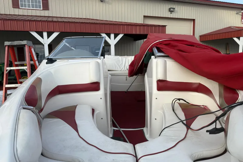 Slide: The Image of 1998 Larson Escape Delta-Conic boat interior with red and white seating, parked near a building. - 16