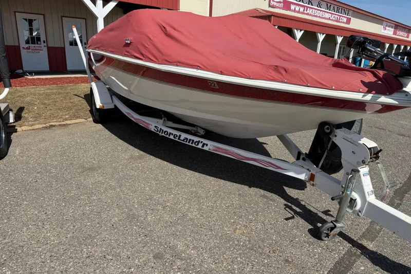 Slide: The Image of 1998 Larson Escape Delta-Conic boat on trailer with red cover, parked outside a marine shop. - 5