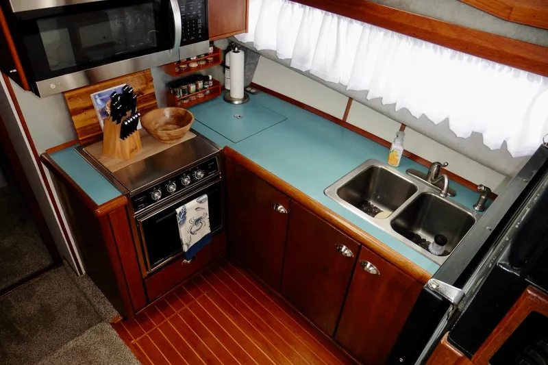 Slide: The Image of 1988 Bayliner 3888 Motoryacht kitchen with stove, microwave, dual sink, and wooden cabinetry. - 10