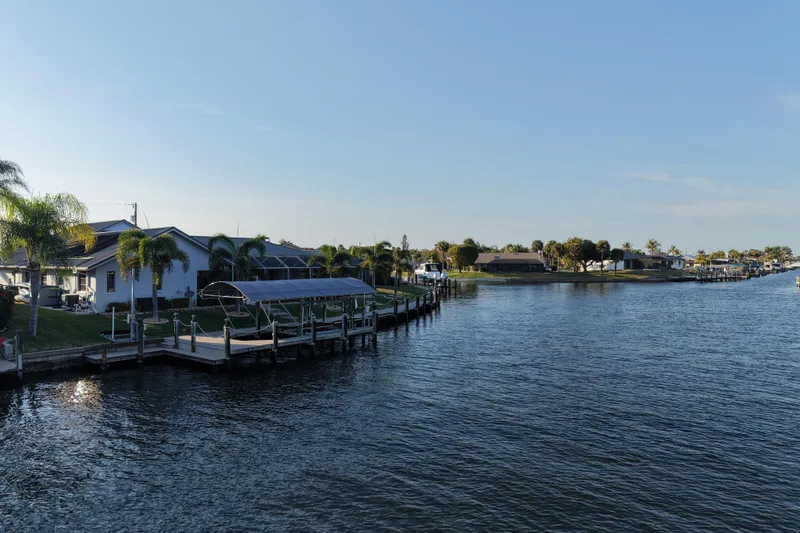 Slide: The Image of Waterfront homes with docks and palm trees along a serene canal under a clear blue sky. - 27