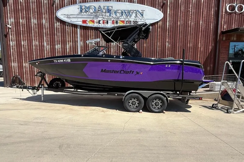 The Image of 2023 MasterCraft XStar S Piranha boat on trailer, purple and black design, parked at Boat Town. - 0