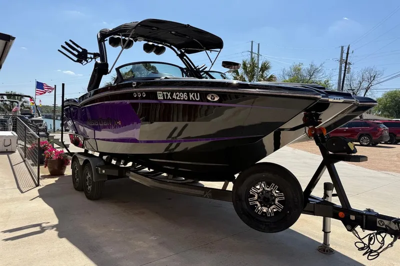 Slide: The Image of 2023 MasterCraft XStar S Piranha boat on trailer, parked outdoors, with American flag in background. - 2