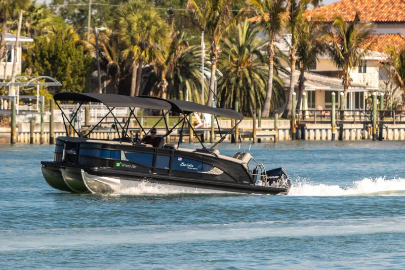 Slide: The Image of 2024 Barletta L23U pontoon boat cruising on a sunny waterfront with palm trees. - 13