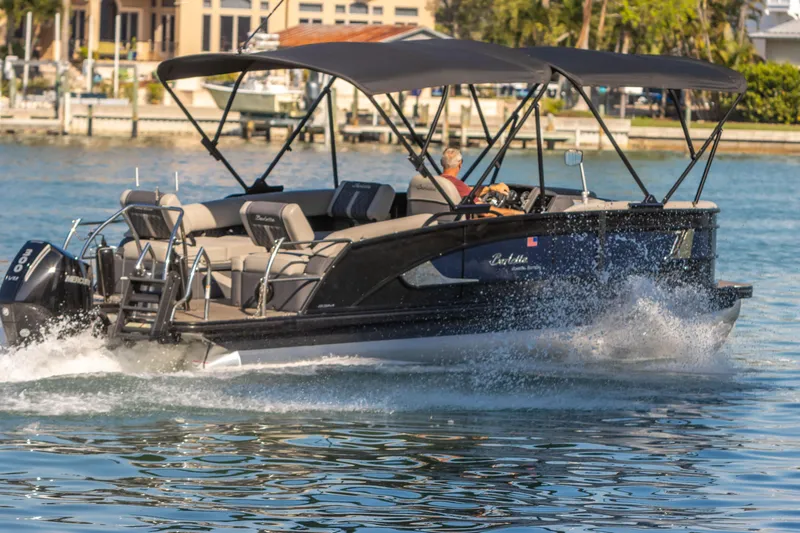 Slide: The Image of 2024 Barletta L23U pontoon boat cruising on water with canopy and seating. - 16