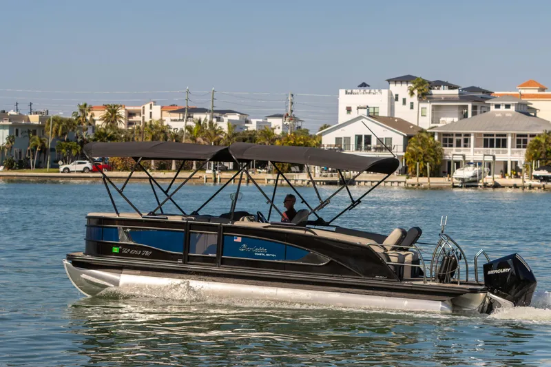 Slide: The Image of 2024 Barletta L23U pontoon boat cruising on a sunny waterfront with modern homes in the background. - 4