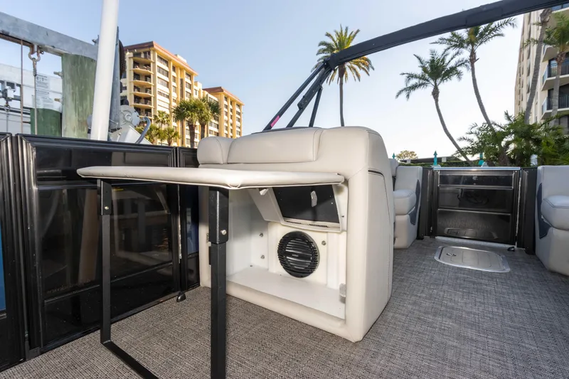 Slide: The Image of 2024 Barletta L23U boat interior with seating, table, and speaker, docked near palm trees. - 49