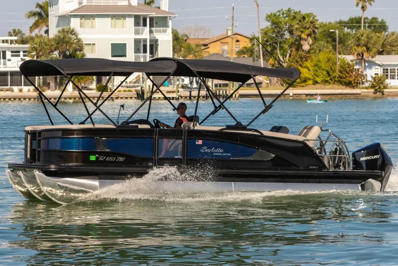 Slide: The Image of 2024 Barletta L23U pontoon boat cruising on water near coastal homes. - 5