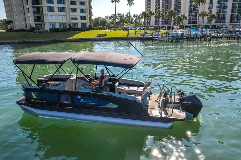 Slide: The Image of 2024 Barletta L23U pontoon boat cruising on a sunny waterfront near modern buildings. - 85