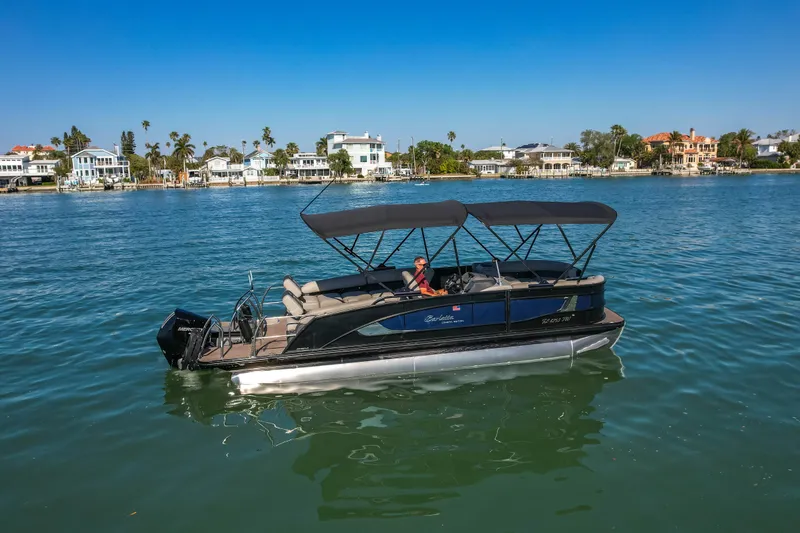 Slide: The Image of 2024 Barletta L23U pontoon boat cruising on a scenic waterfront with luxury homes. - 89
