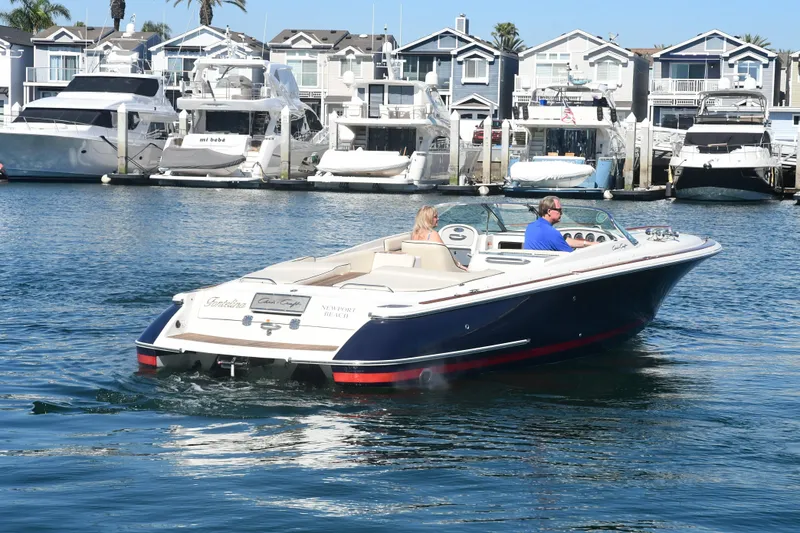 Slide: The Image of 2005 Chris-Craft Corsair 28 cruising in a marina with docked yachts and waterfront homes. - 2